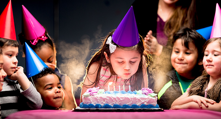 Girl blowing out birthday candles as guests look on